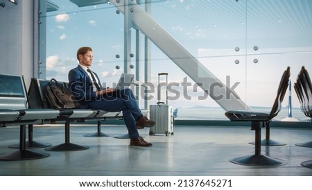 Airport Terminal: Businessman Uses Laptop Computer, Waiting for Flight to International Conference. Traveling Entrepreneur Remote Work Online Sitting in a Boarding Lounge of Airline Hub with Airplanes Royalty-Free Stock Photo #2137645271