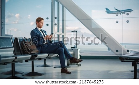 Airport Terminal: Businessman Uses Smartphone, Waiting for a Flight, Doing e-Business, Sending e-Commerce Data. Traveling Man Remote Work Online on Mobile Phone in Boarding Lounge of Airline Hub Royalty-Free Stock Photo #2137645275
