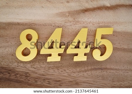 Wooden  numerals 8445 painted in gold on a dark brown and white patterned plank background.