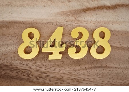 Wooden  numerals 8438 painted in gold on a dark brown and white patterned plank background.