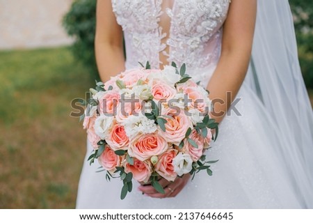A bride with a wedding bouquet of roses and carnations in her hands on the background of a wedding dress