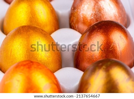 Close-up of Easter painted eggs in gold and bronze in a white package. Selective focus on the middle row.
