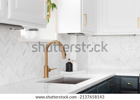 Sink detail shot in a luxury kitchen with herringbone backsplash tiles. white marble countertop, and gold faucet. Royalty-Free Stock Photo #2137658143