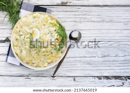 Top view of a bowl of egg salad sandwich spread with fresh boiled eggs and dill over a rustic wood table background. Overhead view.