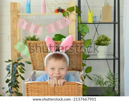 Happy Easter, a cheerful boy with rabbit ears looks out of a wicker basket and hides back.