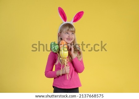 Blonde little girl with Easter eggs on a yellow background