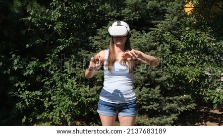 Female in virtual reality glasses controls the device with his hands against the background of green trees