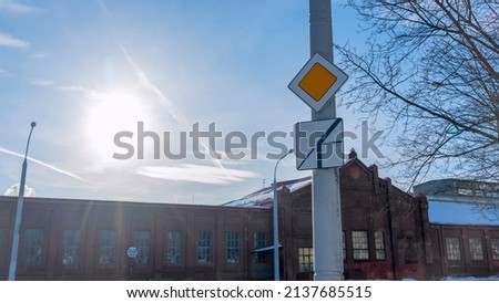 Road sign main road in sun beams against blue sky with clouds. Priority road sign on the background of sky and old building. Road rules concepts.