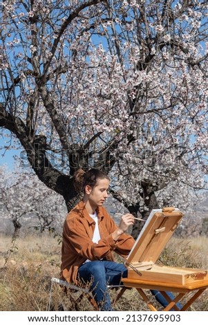 Young man sitting and painting under a tree in spring time in blue sky