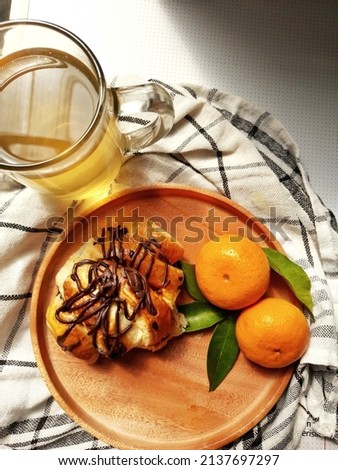 Chocolate croissant and prepared in a brown wooden pallet on a background of herbal drink and citrus fruit for breakfast in the morning