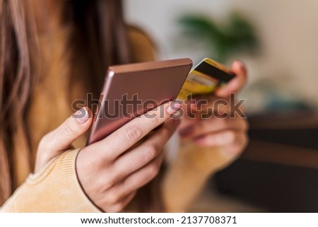 Picture of a young girl, using her credit card and phone to make a purchase.