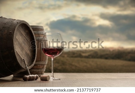 Red wine glass, barrel and corkscrew on a wooden table and vineyard in the background Royalty-Free Stock Photo #2137719737