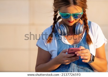 Young woman with headphones and sunglasses using cell phone