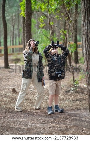 Mother and son getting ready to take pictures in forest. Family with modern cameras using binoculars, standing. Parenting, family, leisure concept