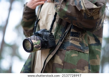 Close-up of modern black camera. Digital camera with big lens on lace against coat in military style. Technology, hobby concept
