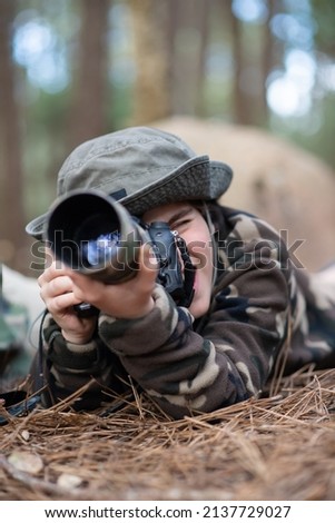 Happy boy taking pictures in forest. Son with modern camera lying on ground, pointing camera. Childhood, hobby, leisure concept