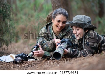 Interested family taking pictures in forest. Mother and son with modern cameras lying on ground, holding cameras, looking at pictures. Parenting, family, leisure concept