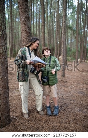 Contented family with cameras walking in forest. Dark-haired mother and son in coats getting ready to take pictures, discussing route. Parenting, family, leisure concept
