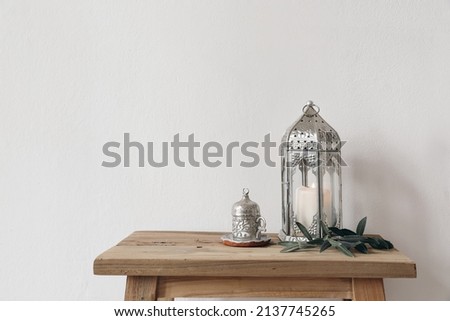 Ramadan Kareem still life. Ornamental lantern with burning candle and Turkish silver cup with tea or coffee. Green olive tree branches on old wooden table background. Muslim Iftar dinner. No people Royalty-Free Stock Photo #2137745265
