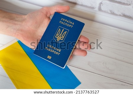 Man hand holding ukrainian passport near blue yellow national Ukraine flag on white wooden background. Top view, flat lay. Stand wirh Ukraine