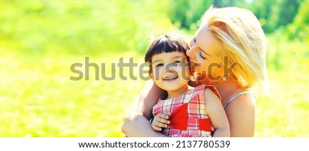 Portrait of happy young mother kissing her little baby walking outdoors in summer sunny park, banner blank copy space for advertising text