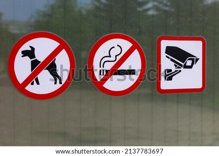 Signs on the outer glass of the office building prohibiting smoking and entry with dogs, warning about video filming by a surveillance camera. Background with copy space for text