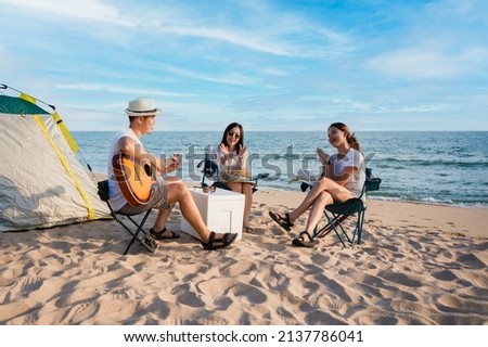 Group of happy Asian friends playing guitar and singing with clap while picnic and camping on the beach in outdoors vacation summer. Young male, female tourist smile fun at party near tent on seaside. Royalty-Free Stock Photo #2137786041