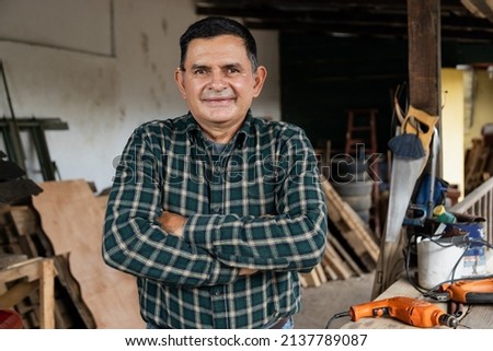 Hispanic carpenter smiling proud in wood shop of him - Proud owner of carpentry shop standing with arms crossed Royalty-Free Stock Photo #2137789087