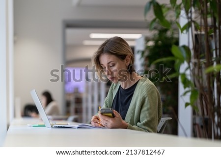 Pensive focused middle-aged woman university teacher using laptop while preparing materials for upcoming lecture, female freelancer working remotely in total silence of public library, selective focus