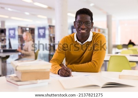 Portrait of happy african-american male student working with book in public library. High quality photo