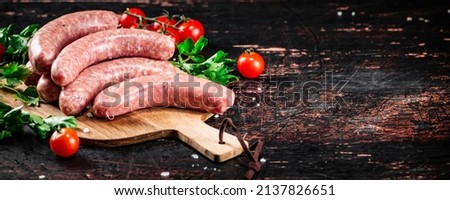 Raw sausages on a wooden cutting board with tomatoes and herbs. Against a dark background. High quality photo