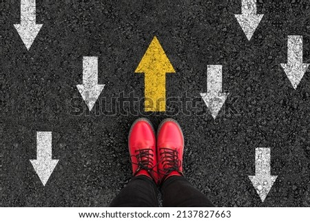 woman boots on asphalt and opposing direction arrows on asphalt ground, personal perspective footsie concept for finding your own way  Royalty-Free Stock Photo #2137827663