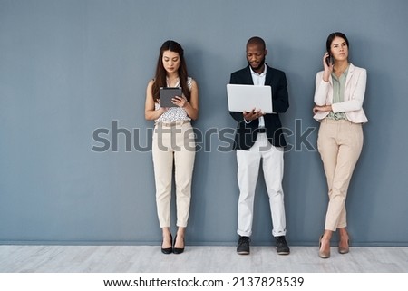 Busy making success happen with their connections. Shot of a group of businesspeople using digital devices while standing in line against a grey background.