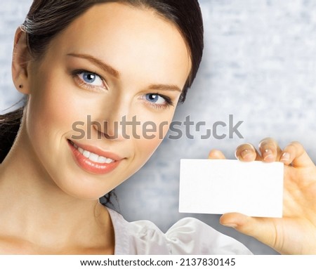 Closeup portrait of smiling businesswoman showing mockup empty businesscard or plastic credit card, with copy space for sign. Brunette business woman at studio image. White bricks wall.