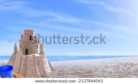 Sand castle on the seashore. Next to it is a blue plastic baby bucket and a red baby shovel
