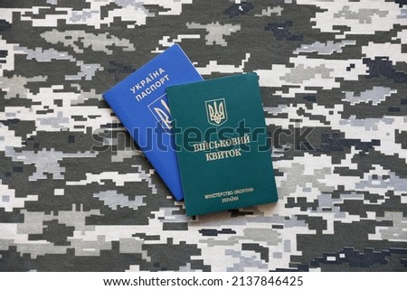 Ukrainian military ID and foreign passport on fabric with texture of pixeled camouflage. Cloth with camo pattern in grey, brown and green pixel shapes with Ukrainian army personal token and passport.