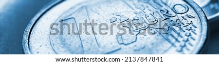 Euro coins. The focus is on the inscription with the name of the Eurozone currency on the 1 euro coin. Close-up. Blue tinted banner or headline about the economy news of the European Union. Macro Royalty-Free Stock Photo #2137847841