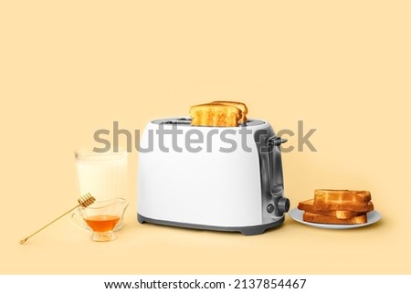 Modern toaster with bread slices, glass of milk and honey on beige background