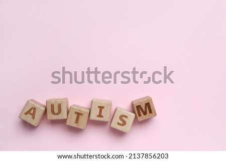 Wooden cubes with word AUTISM on pink background