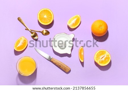 Ceramic juicer, knife, spoons and oranges on purple background
