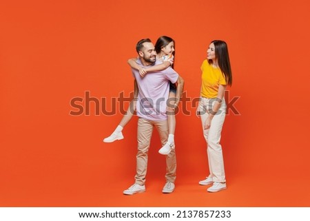 Full body young fun happy parents mom dad with child kid daughter teen girl in basic t-shirts giving piggyback to daughter isolated on yellow background studio Family day parenthood childhood concept.
