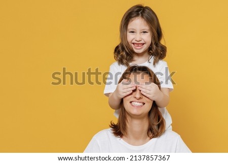 Happy woman in white t-shirt have fun with cute child baby girl 5-6 years old cover face. Mommy little kid daughter isolated on yellow orange color background studio. Mother's Day love family concept