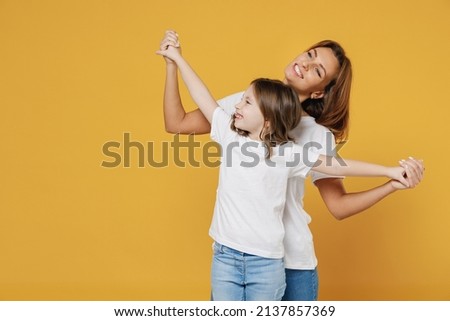 Happy woman in basic white t-shirt have fun dance cute child baby girl 5-6 years old. Mommy mum little kid daughter isolated on yellow orange color background studio. Mother's Day love family concept