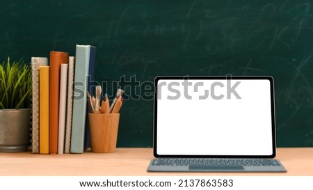 Education space concept, Laptop computer white screen mockup for montage your graphic on screen, stack of books, decor plant and stationery against green chalkboard background.