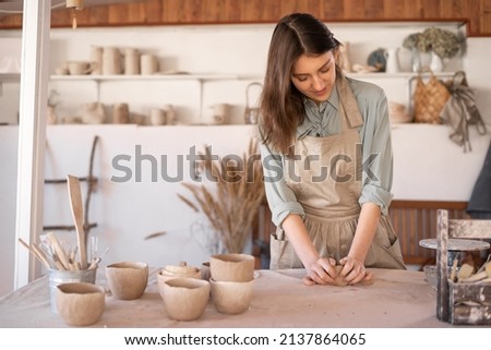 Young beautiful woman with long hair in an apron creates a handmade ceramic bowl from clay. Creative workshop. The concept of skill and entrepreneurship. copy space.