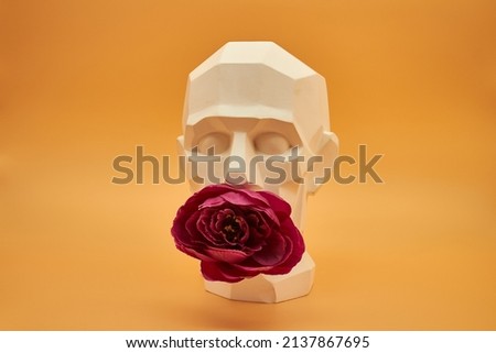 Plaster faceted male head with red flowers on a yellow beige background