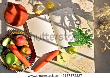 Open notebook decorated by apples, carrots, pumpkin and leaves. top view