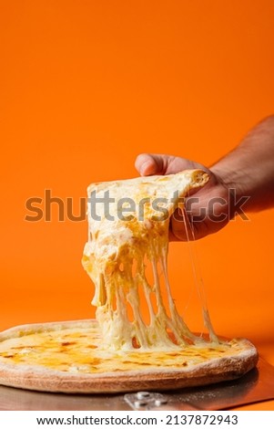 The hand pulls a cheese pizza. Mozzarella, gouda, camembert, cheddar and cream sauce. Orange background.