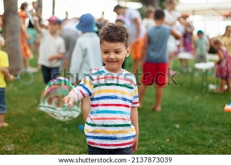 An emotional boy with a big bubble. Summer weekend, recreation, children's animation in the park in the fresh air, animation program with soap bubbles. Royalty-Free Stock Photo #2137873039