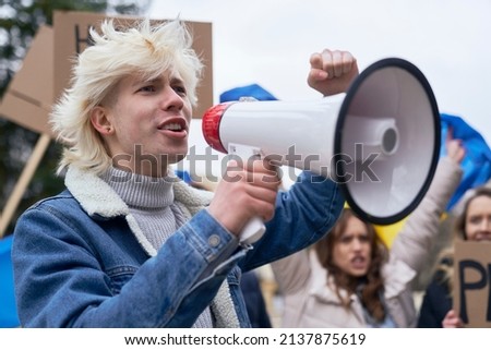 Close up of caucasian man  screaming through megaphone in front and group of people manifesting  in the background
